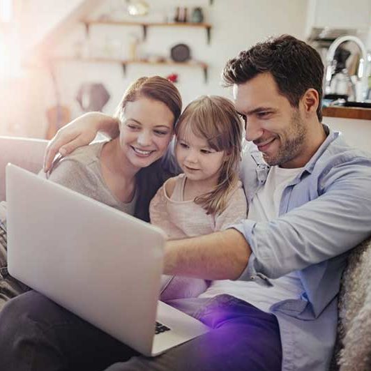 A family sits on their couch with a laptop 